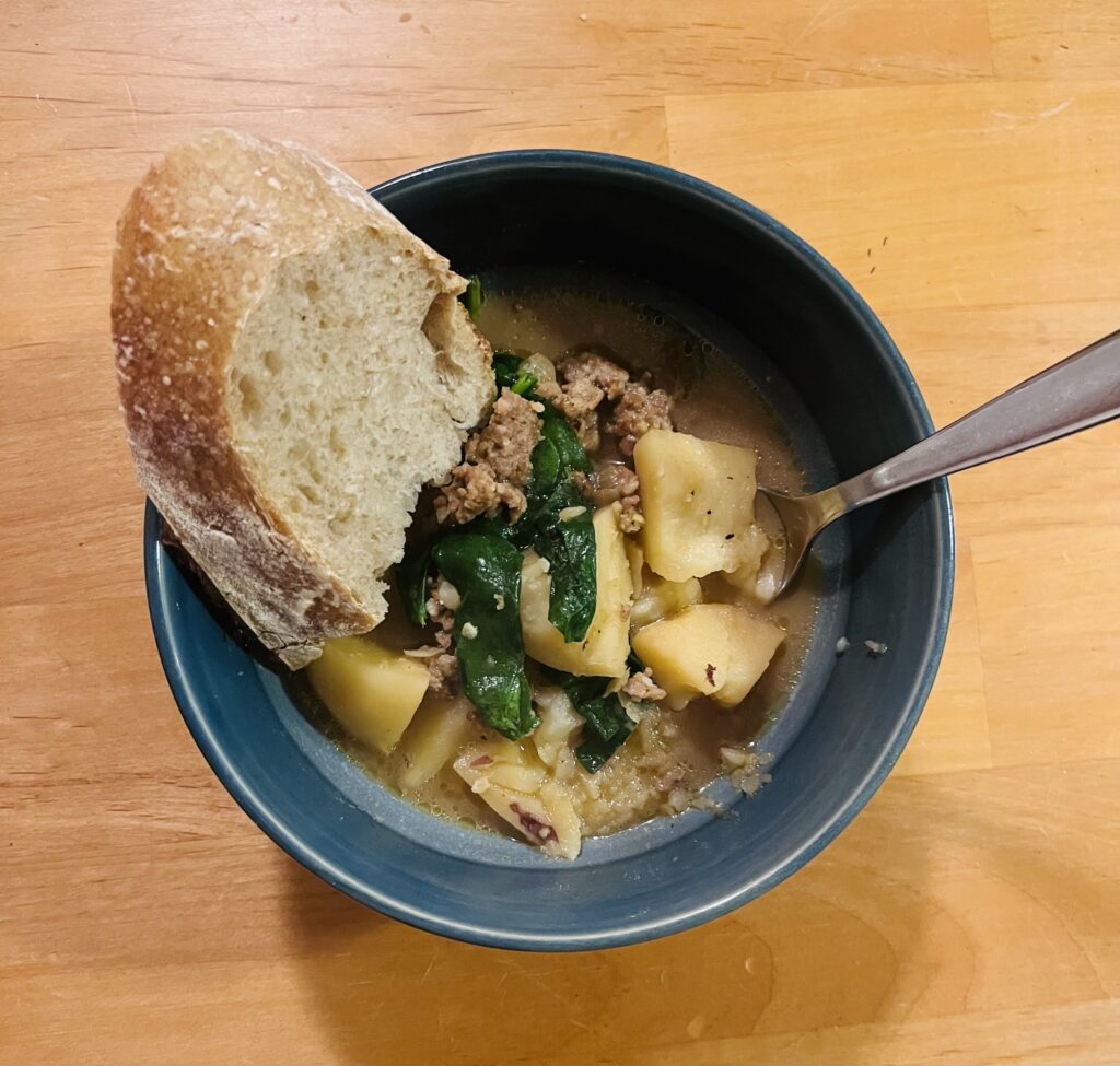 Sausage, potato and spinach soup served in a bowl with a piece of bread