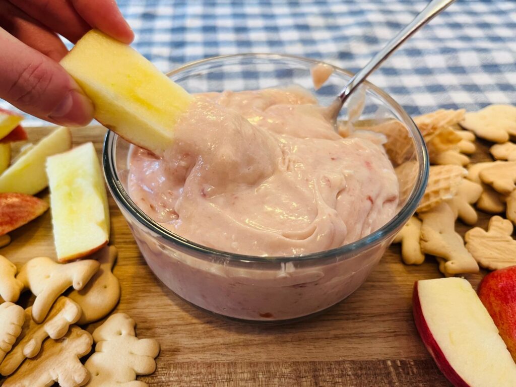 apple slice being dipped into the strawberry cheesecake dip