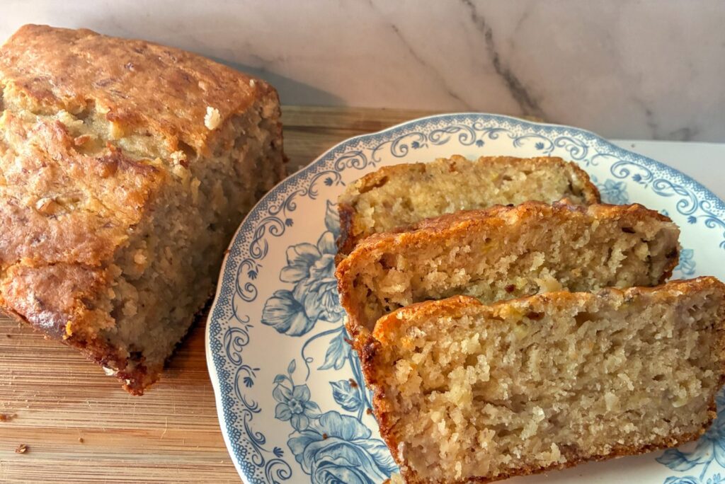 Three slices of banana bread on a plate with a half loaf next to it