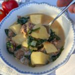 sausage and potato soup being scooped out of a small bowl with tomatoes next to it