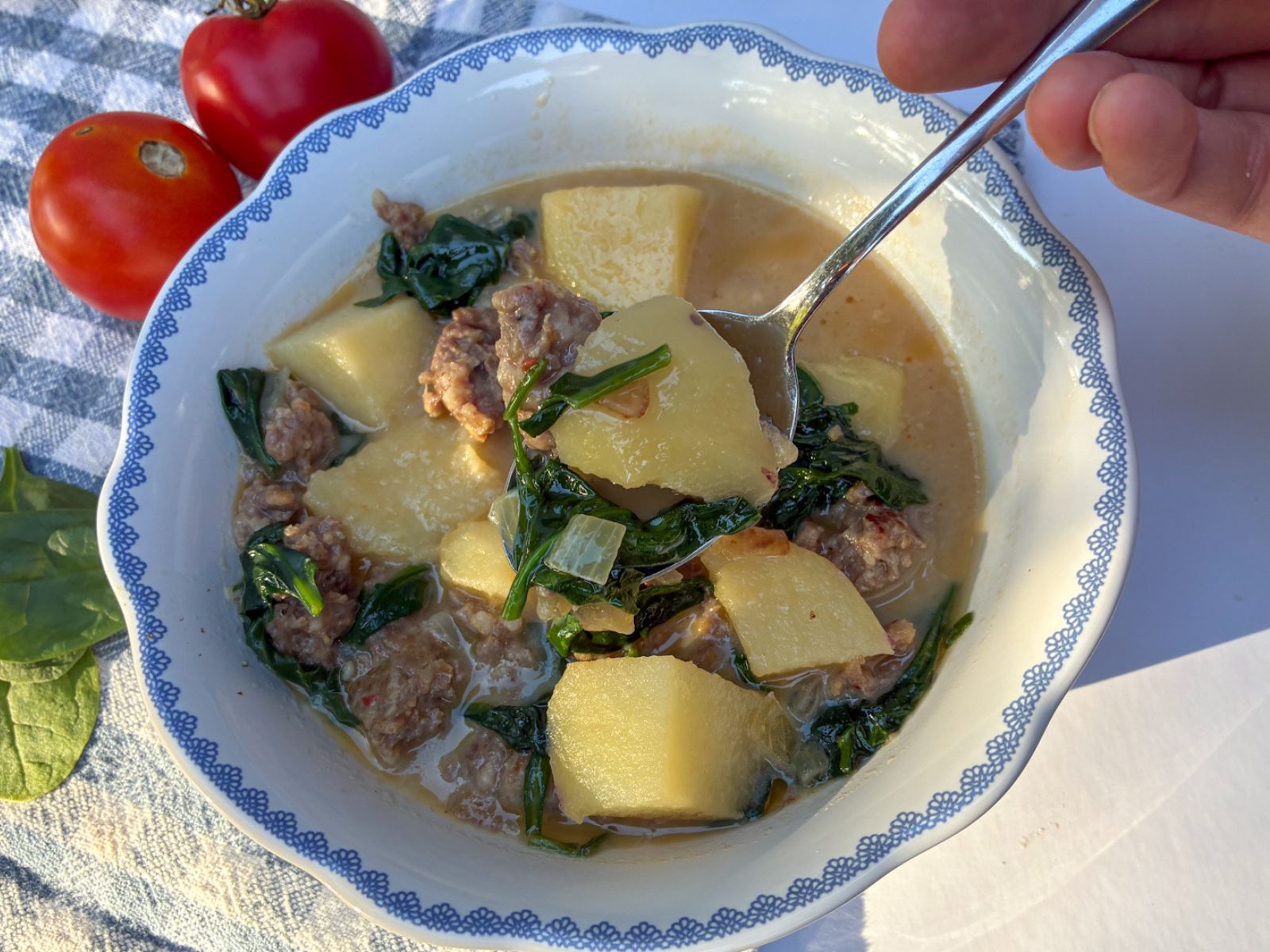 sausage and potato soup being scooped out of a small bowl with tomatoes next to it