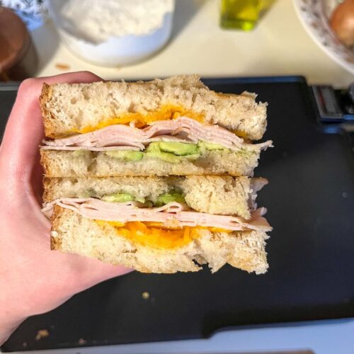 sourdough turkey melt cut in half and being held in a hand above a griddle