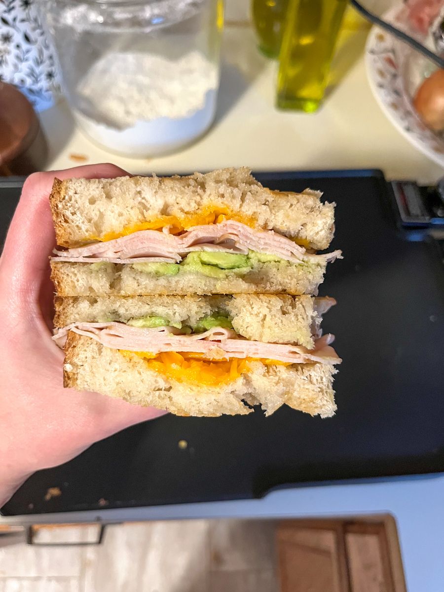 sourdough turkey melt cut in half and being held in a hand above a griddle