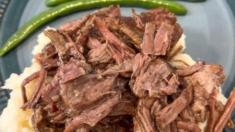 Mississippi pot roast on top of potatoes with a side of green beans