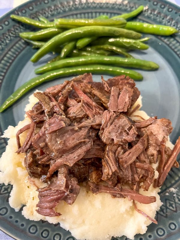 Mississippi pot roast on top of potatoes with a side of green beans