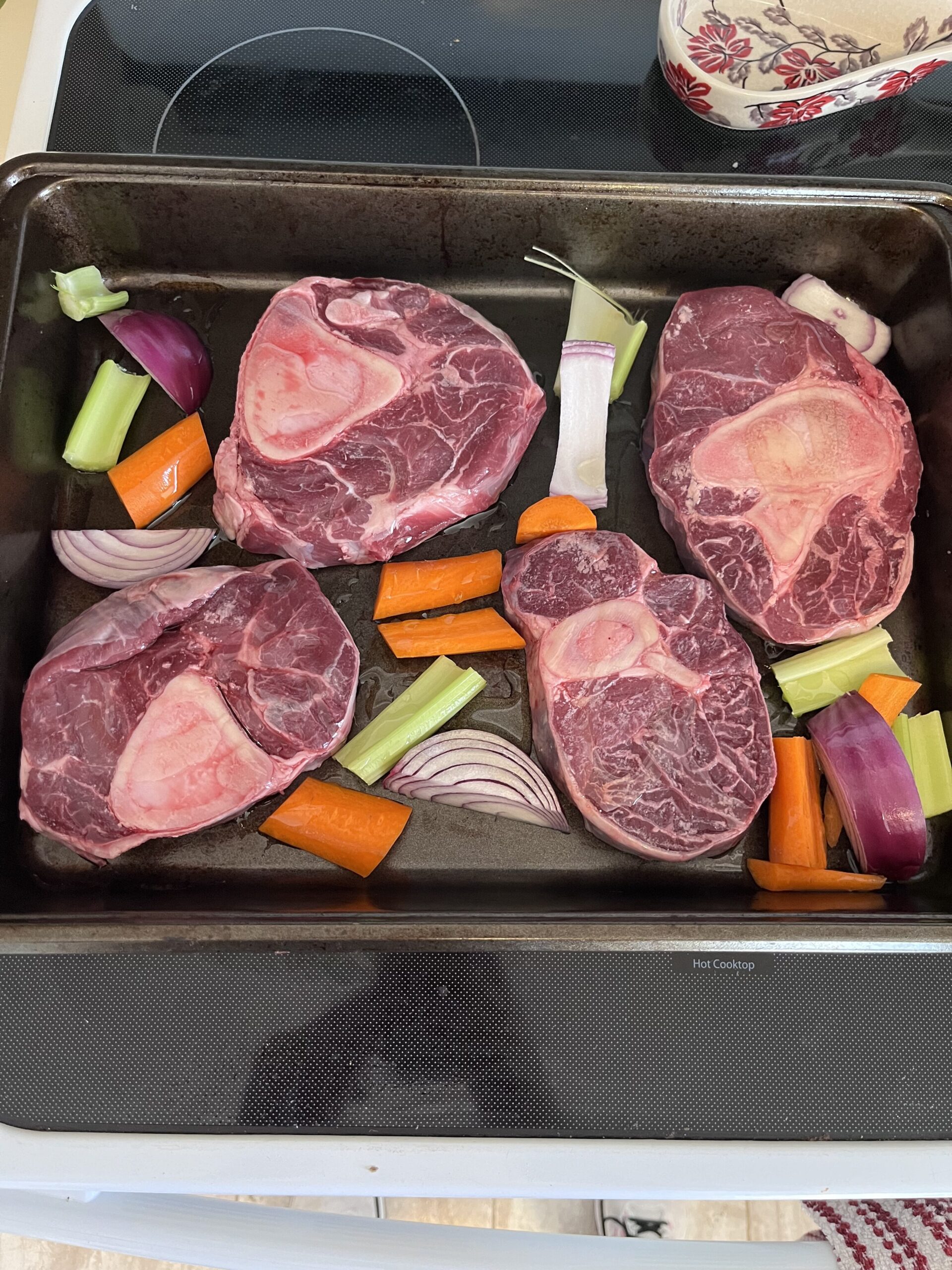 Raw soup bones and vegetables on roasting pan before being roasted in the oven