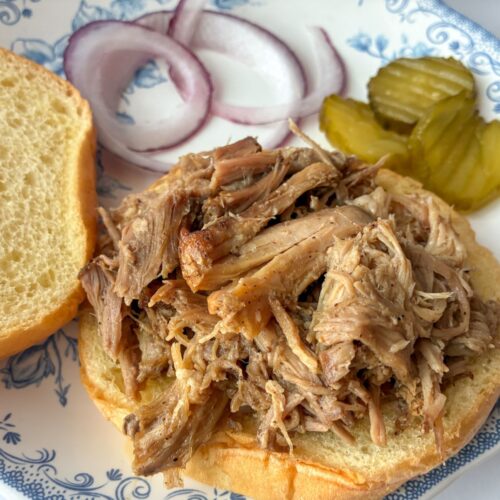Dry rubbed pulled pork served on a sandwich bun with pickles and onions next to it