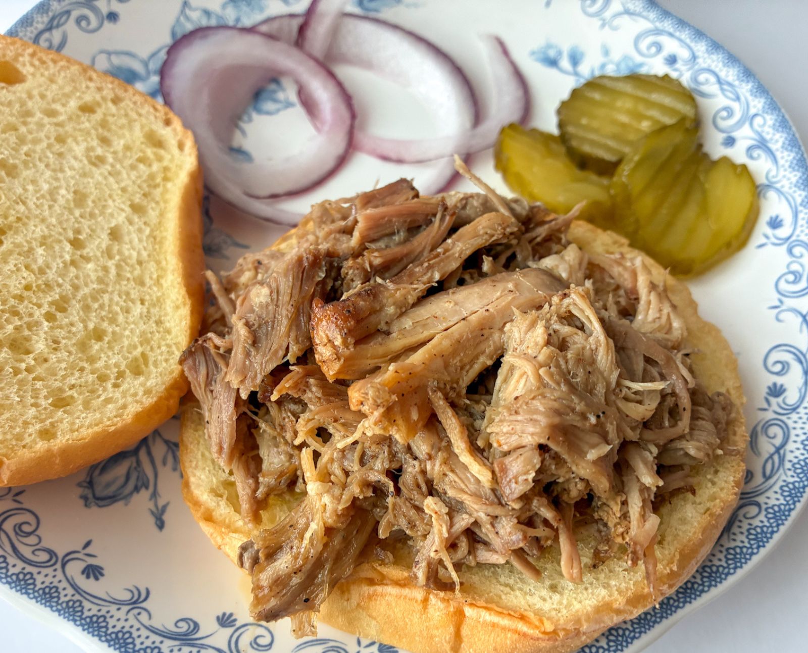 Dry rubbed pulled pork served on a sandwich bun with pickles and onions next to it