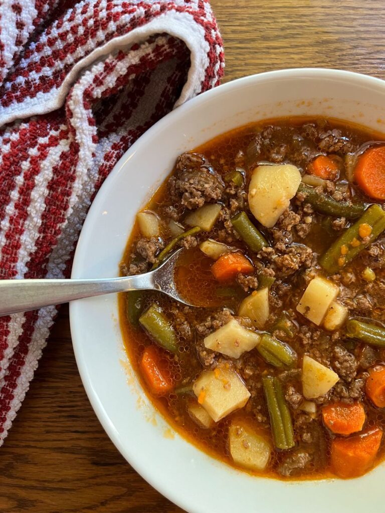 wholesome recipe with bone broth (hamburger soup) in a bowl with a tea towel next to it