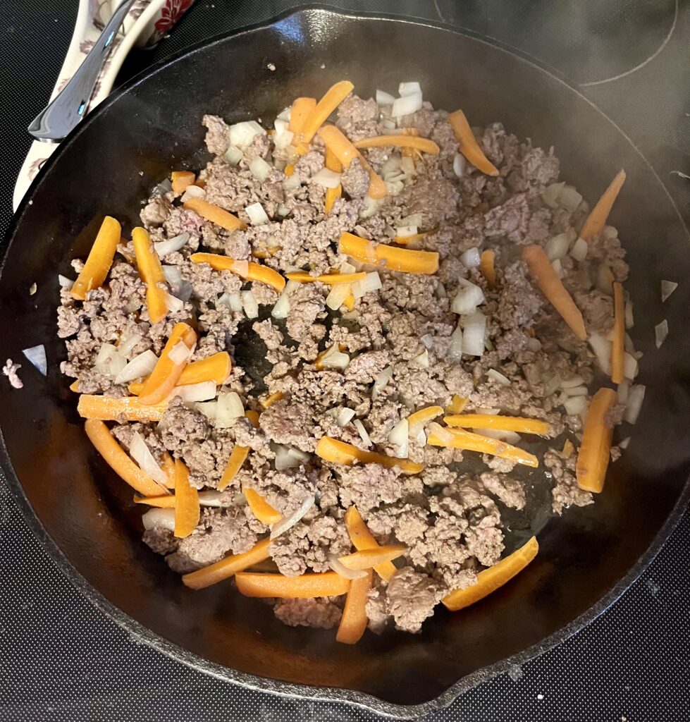 Egg roll in a bowl cooking in a cast iron skillet. The ground beef, onions, and carrots are cooking here.