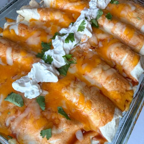 Six pulled pork enchiladas in a pan fresh out of the oven topped with sour cream and cilantro