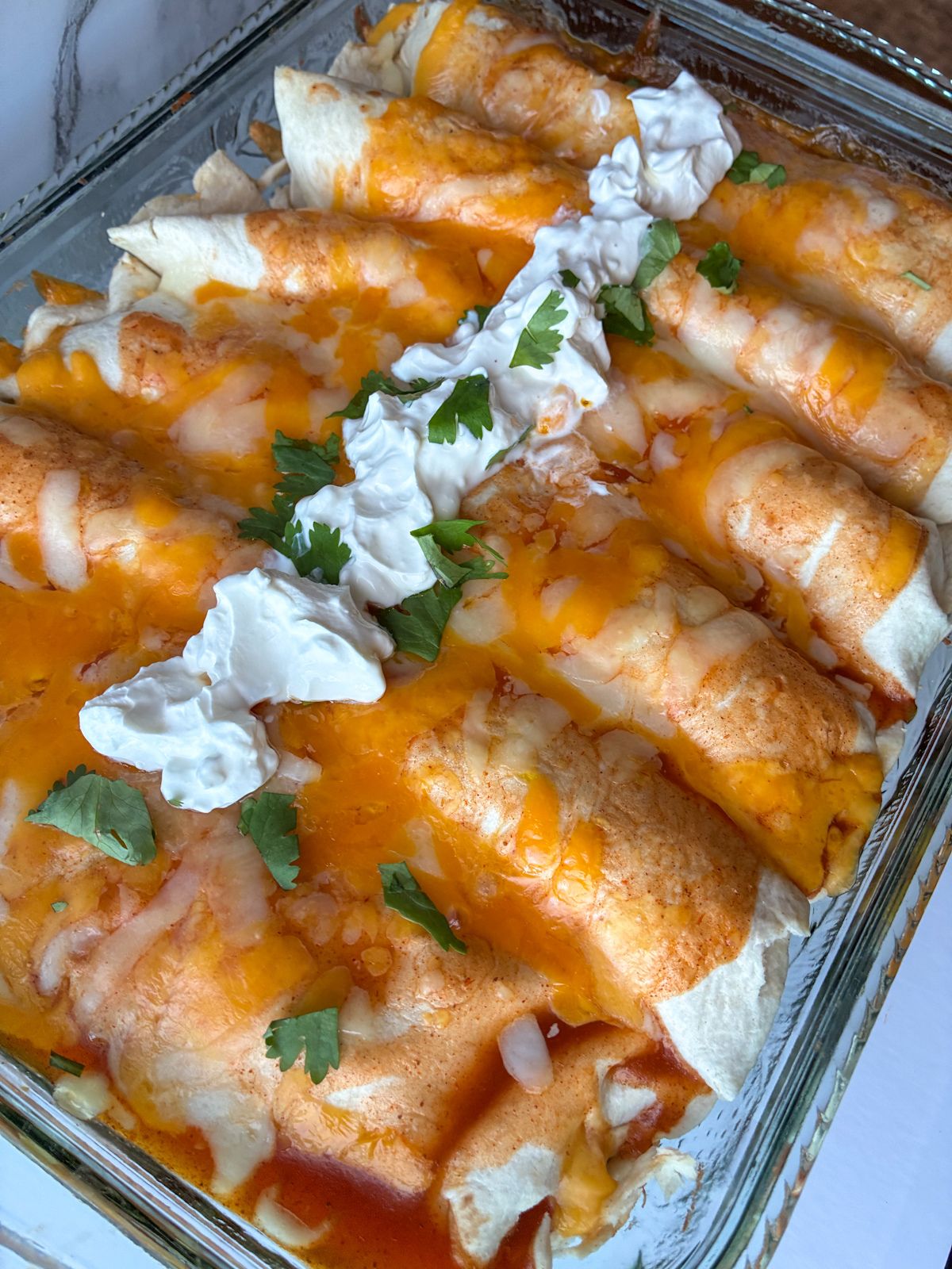 Six pulled pork enchiladas in a pan fresh out of the oven topped with sour cream and cilantro