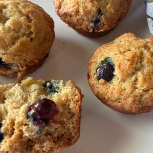 4 sourdough discard muffins laying on a plate. One with a bite out of it.