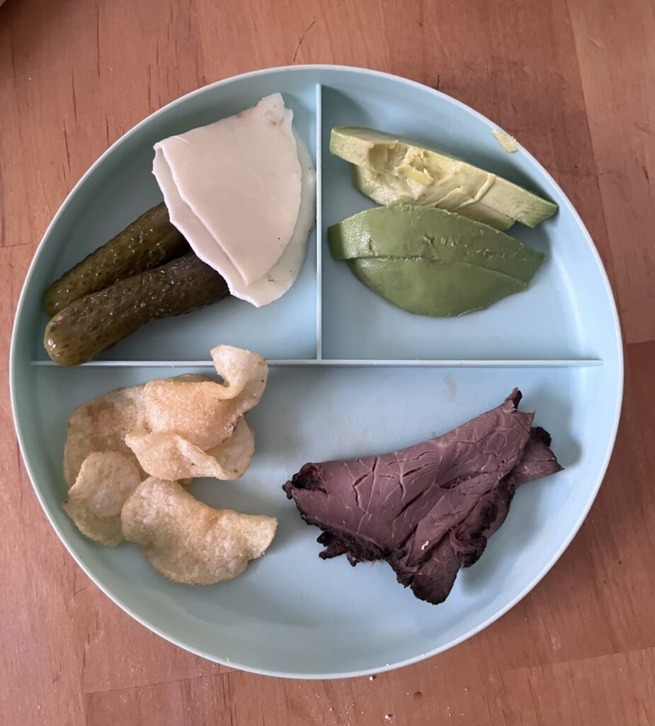 Preschool lunch on plate with sliced roast beef deli meat, chips, provolone cheese, pickles, and avocado