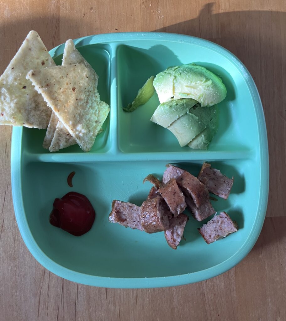 Easy preschool lunch on a plate including chicken sausage, tortilla chips and guacoamole to dip