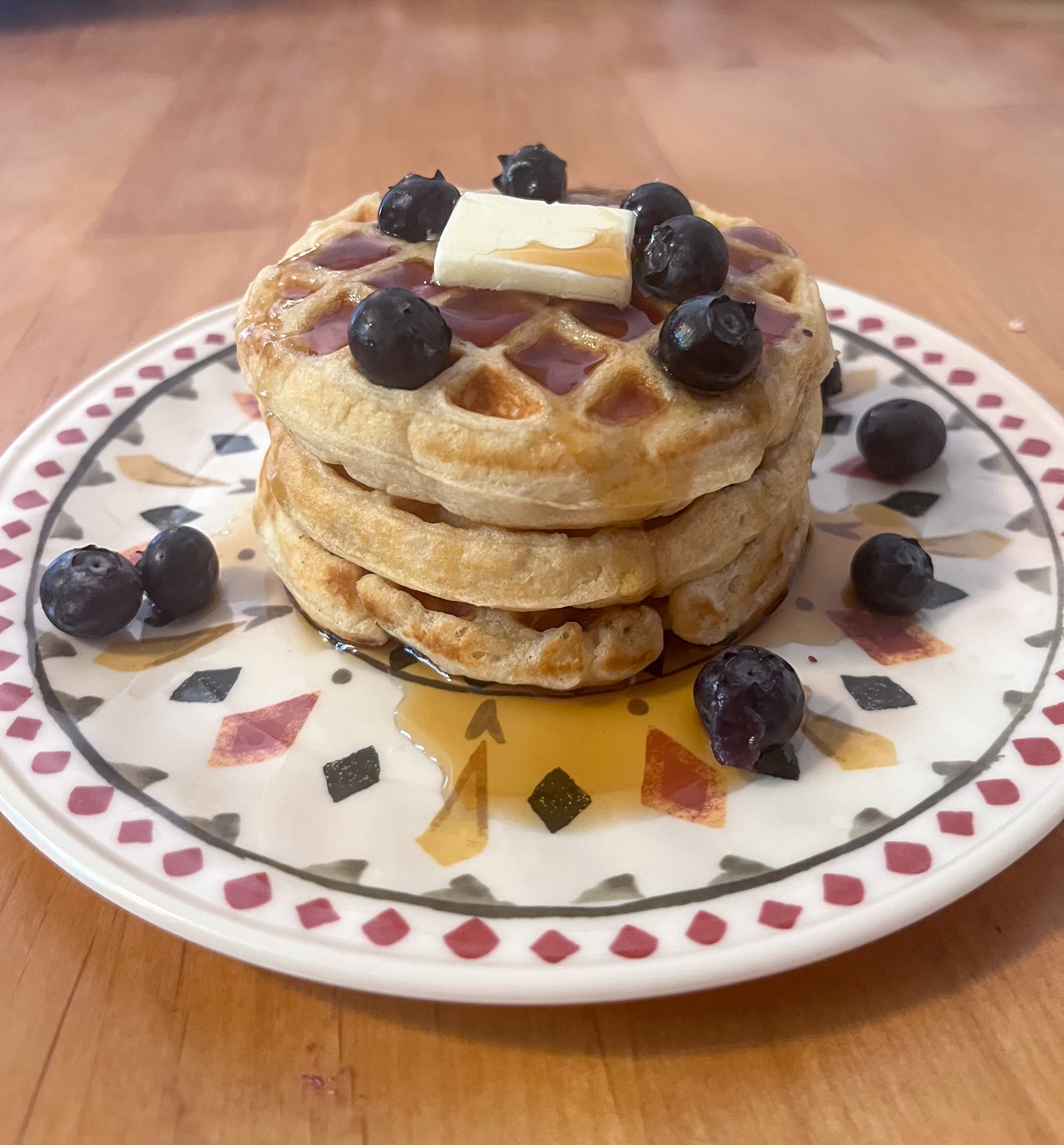 Egg Free Waffles stacked on a plate with blueberries, butter, and maple syrup