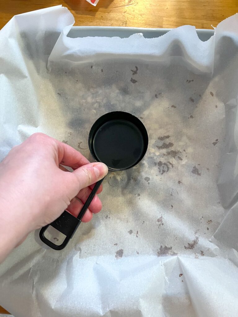 granola bars in a pan being pushed down with a measuring cup
