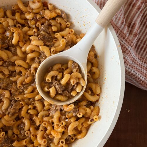 homemade hamburger helper in a large skilled with a spoon scooping it out