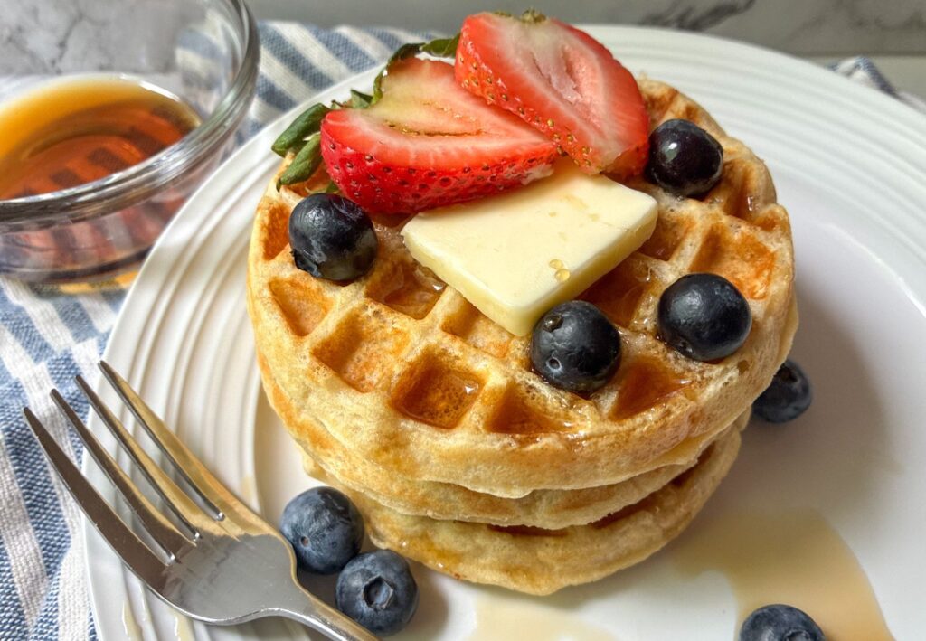 Eggless waffles stacked on top of each other with fresh fruit and a fork on a plate
