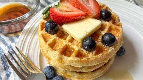 Eggless waffles stacked on top of each other with fresh fruit and a fork on a plate