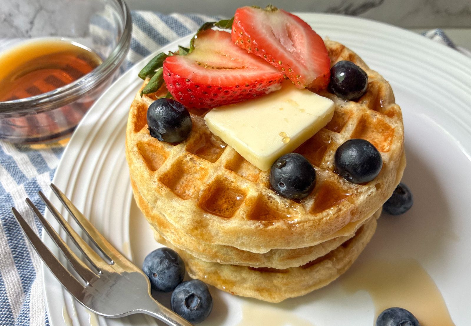 Eggless waffles stacked on top of each other with fresh fruit and a fork on a plate