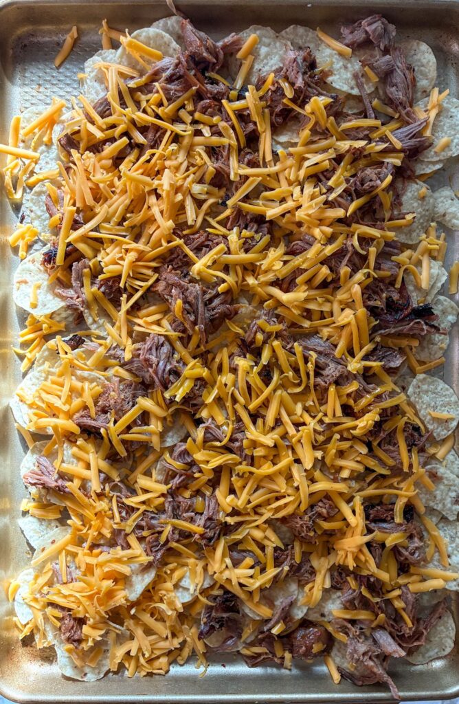Process shot of tortilla chips layered with pulled pork and cheese prior to going into the oven