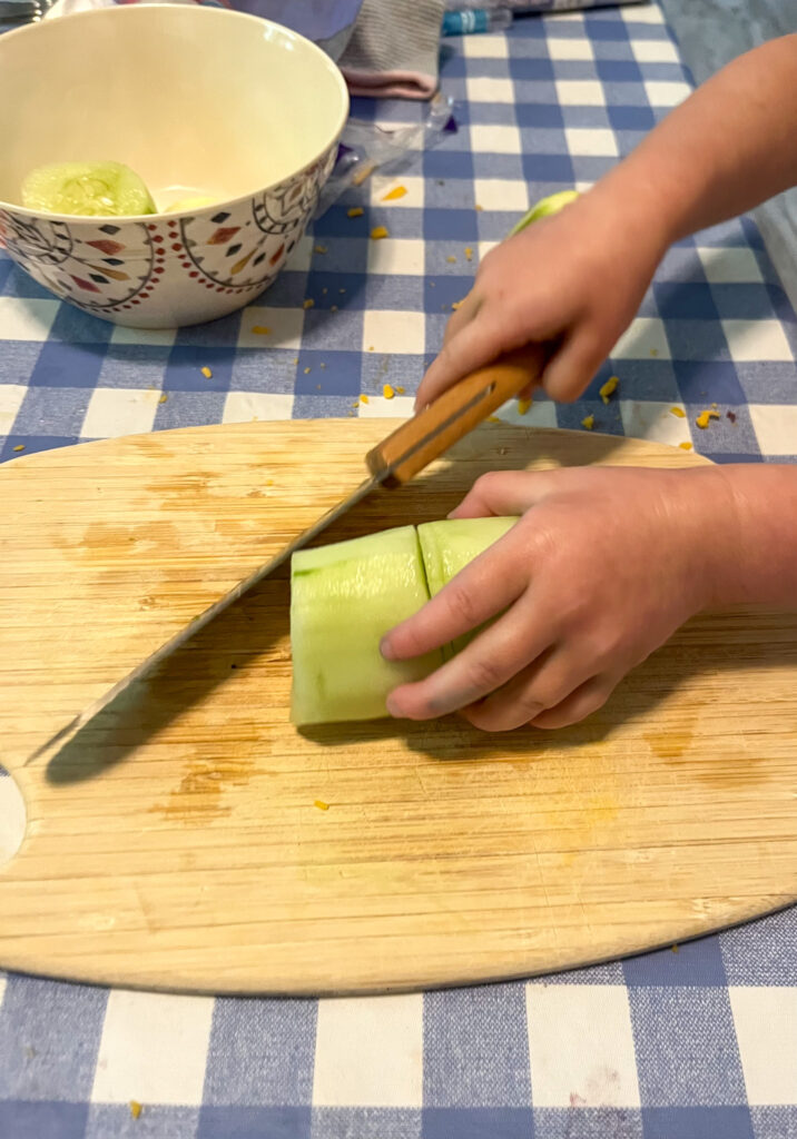 child using the child safe knife and chopping a cucumber