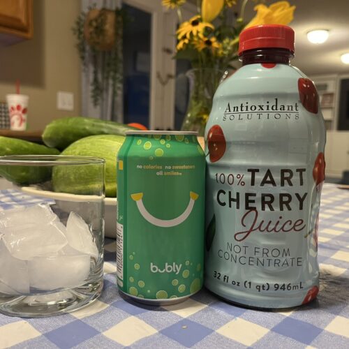 A small glass filled with ice next to a lime bubbly and a jar of tart cherry juice