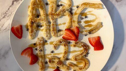 Letters and number pancakes top with powdered sugar, maple syrup and strawberries