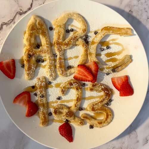 Letters and number pancakes top with powdered sugar, maple syrup and strawberries