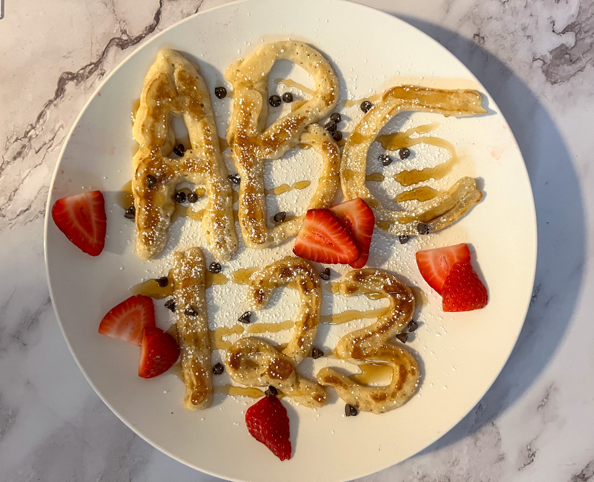 Letters and number pancakes top with powdered sugar, maple syrup and strawberries