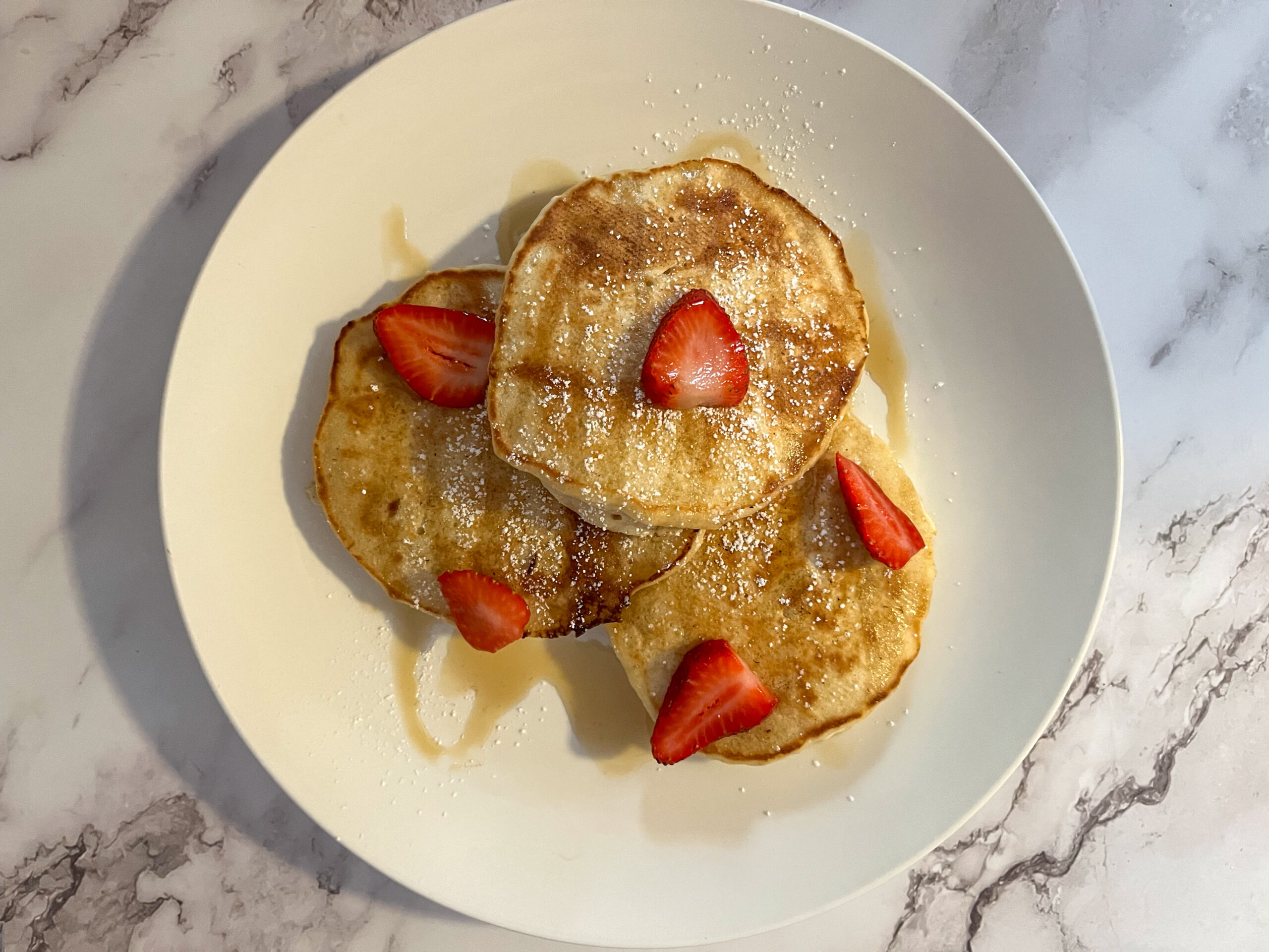 Three egg free pancakes on a plate covered in maple syrup and strawberries