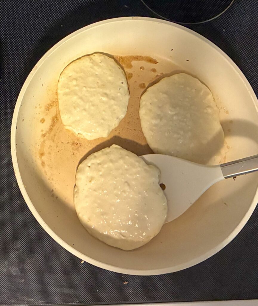 Skillet with 3 pancakes cooking a spatula to flip