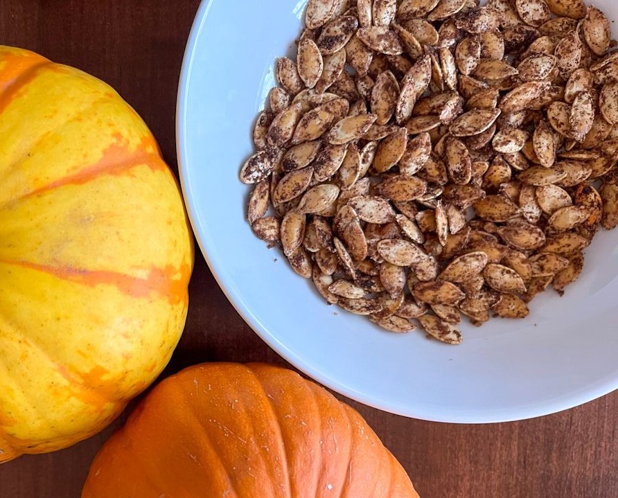 cinnamon sugar pumpkin seeds in a bowl with two pumpkins next to it