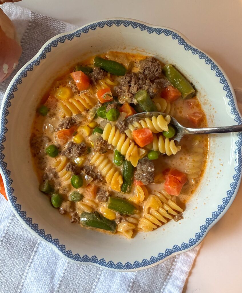 Spoon scooping out noodles and vegetables from a bowl