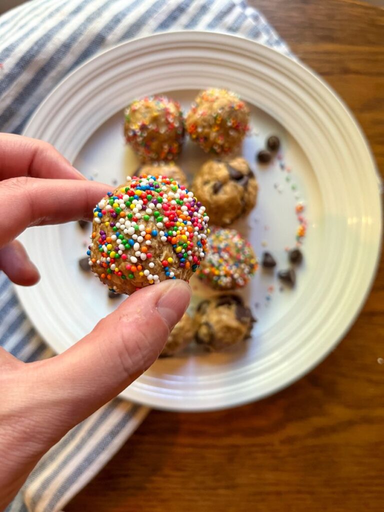 no bake protein balls on a plate with a hand holding up 1 of the balls