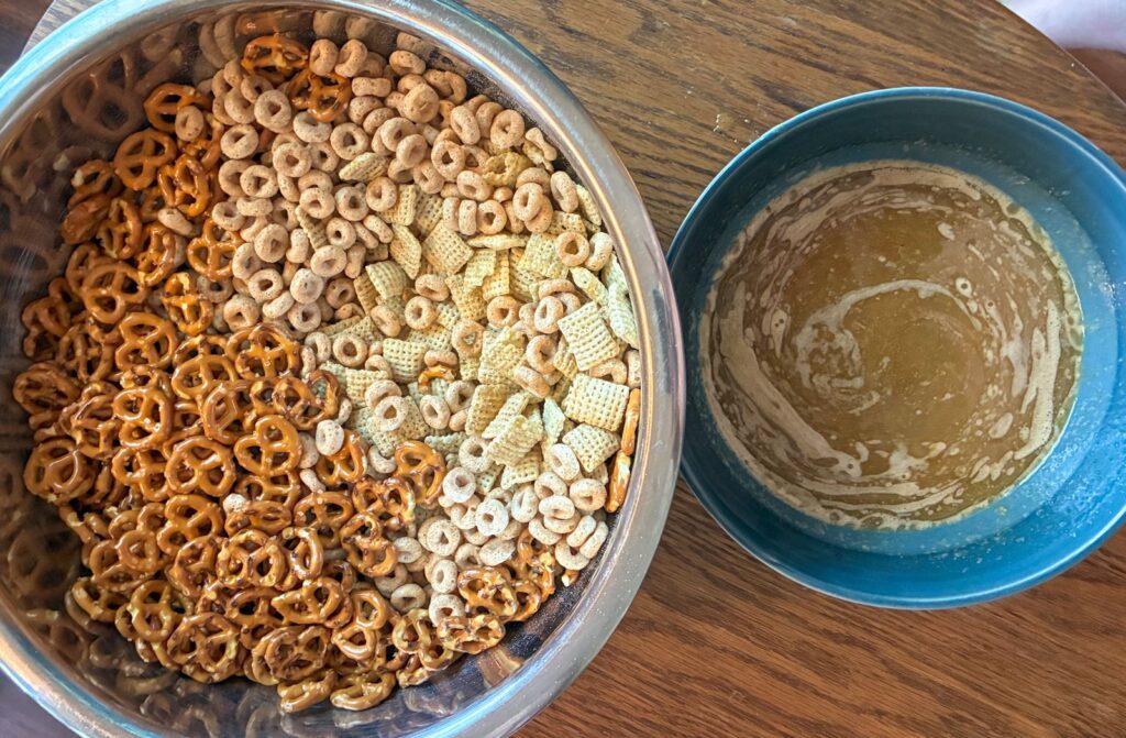 A large bowl on the left with all the cereals and pretzels and a small bowl on the right with the melted butter and spices mixed in.