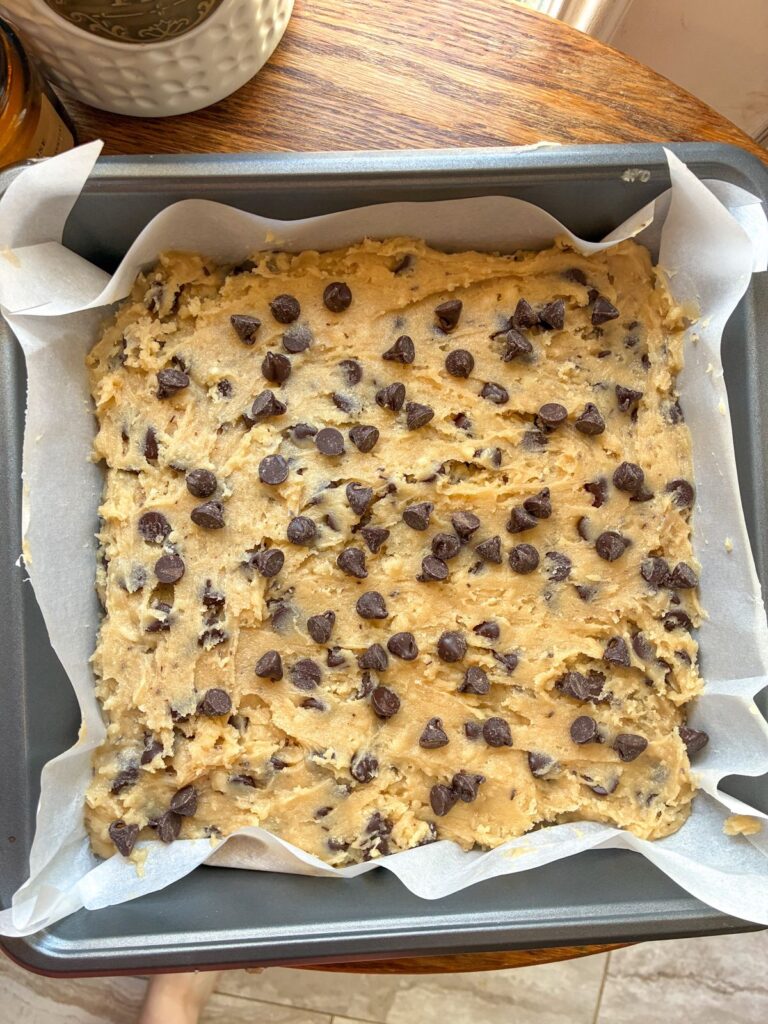 eggless chocolate chip cookie dough in a 9x9 metal baking pan topped with chocolate chips