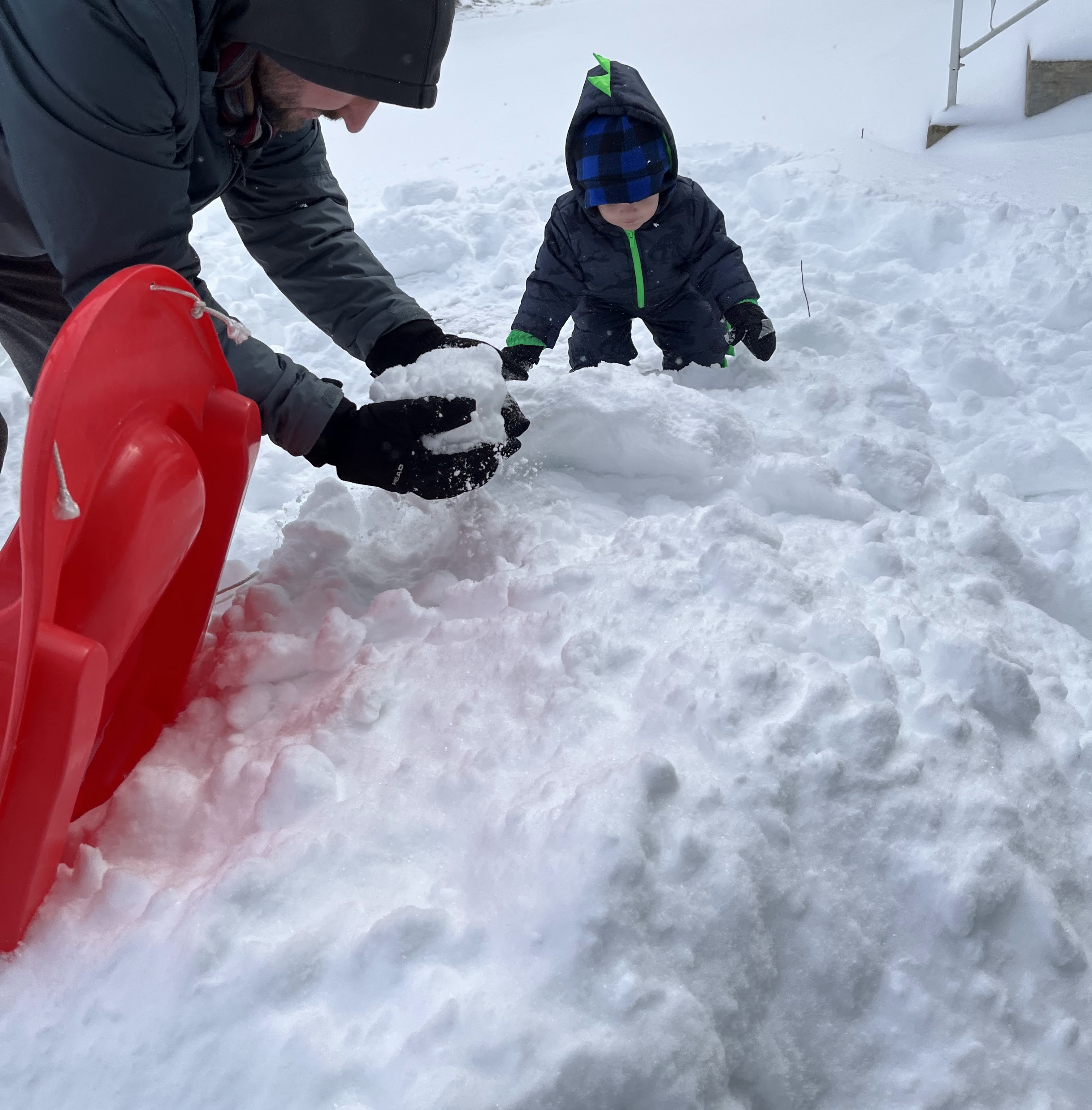 A child and dad playing in the snow together and the dad scooping up a snowball