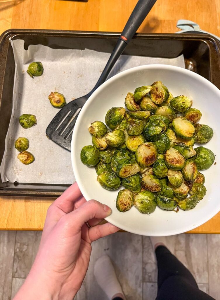 oven roasted brussel sprouts in a bowl being held above the baking sheet