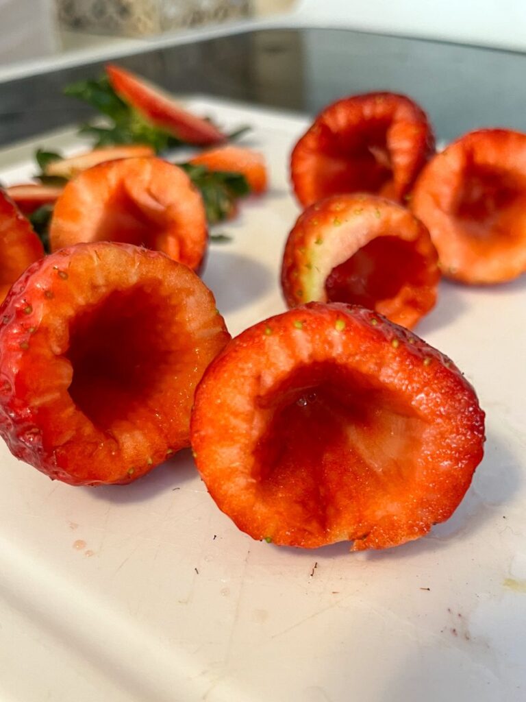 strawberries on a cutting board that have been hulled and hallowed out