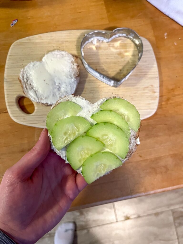 hand holding a the valentines day sandwich with cucumbers and cream cheese on top.