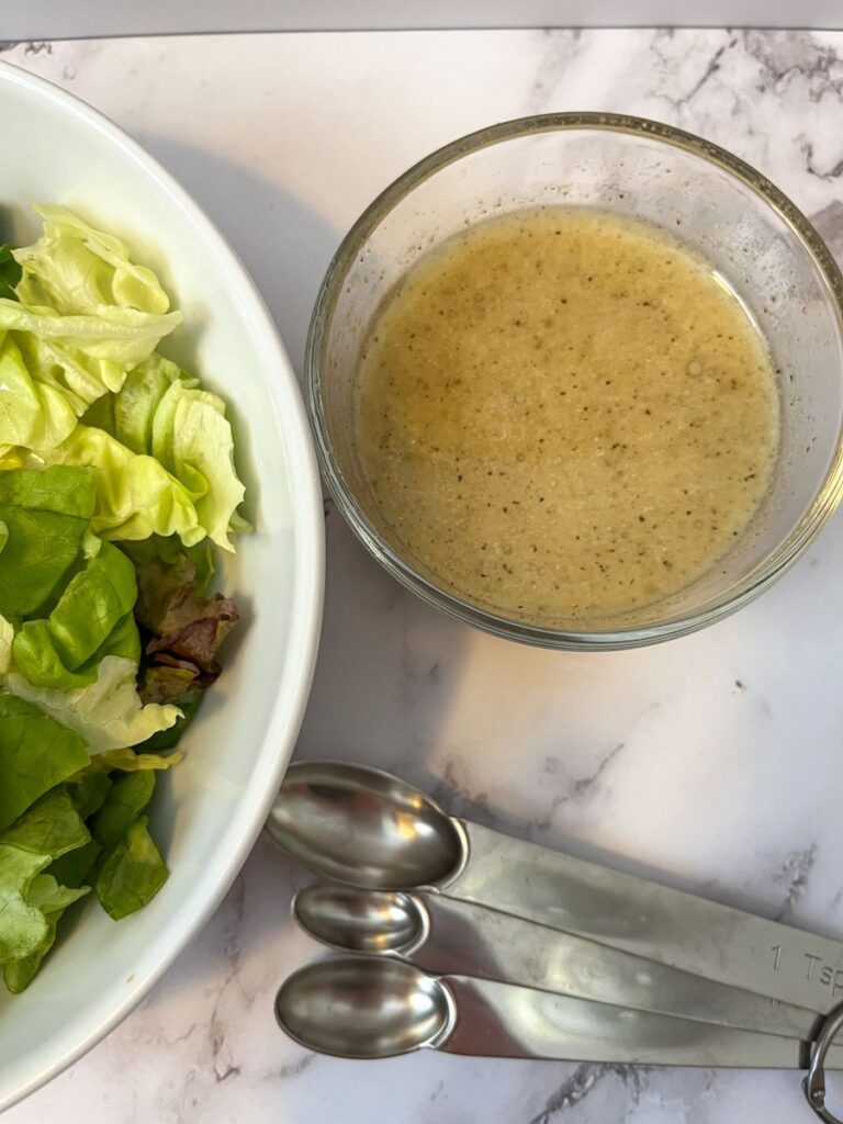 White wine vinaigrette in a small bowl next to a bowl of salad