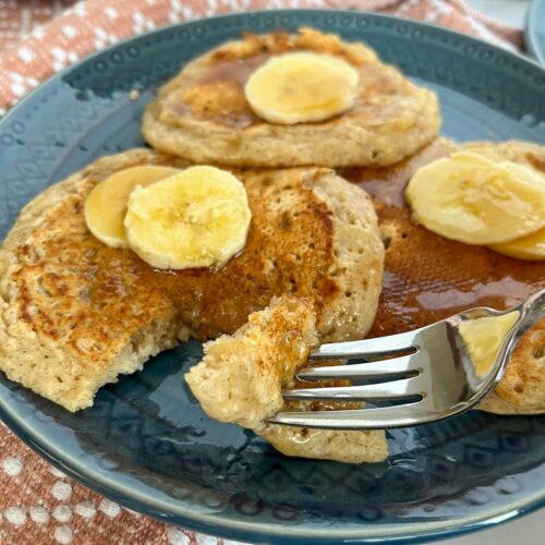 banana pancakes without eggs served on a plate with a bite taken out. Topped with sliced bananas.