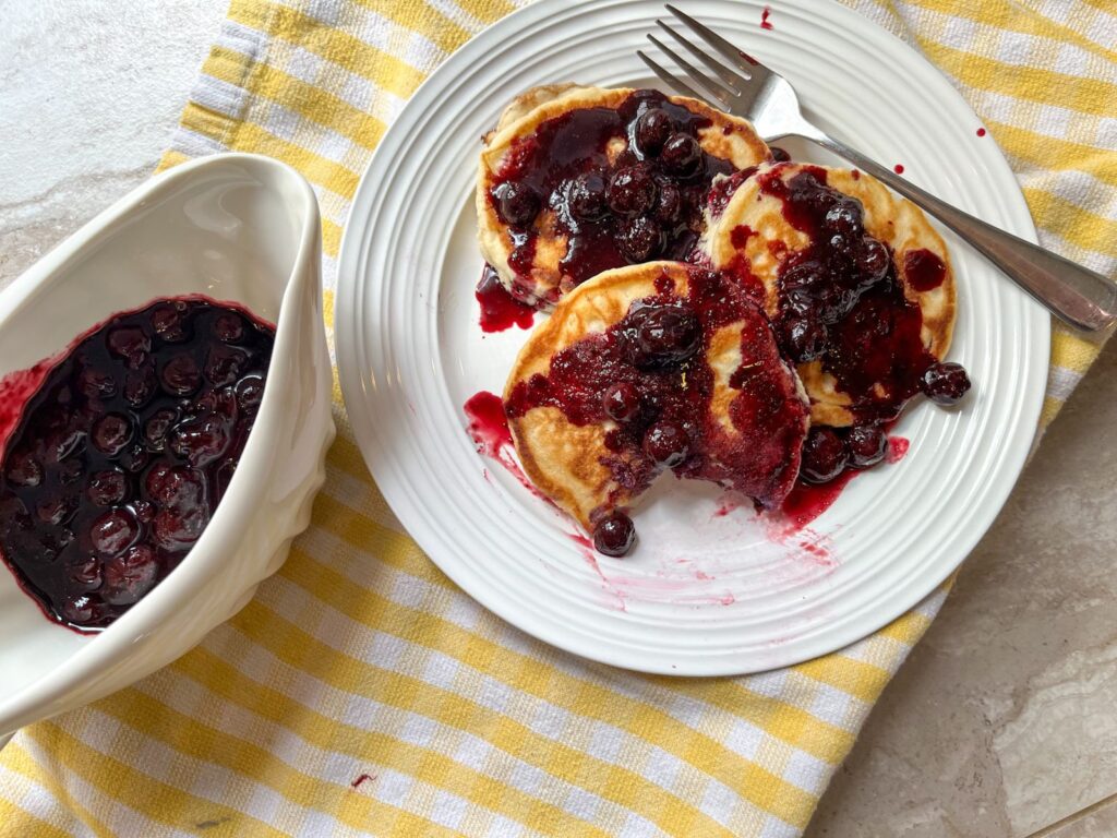 3 pancakes covered in blueberry maple syrup and a dish filled with the syrup