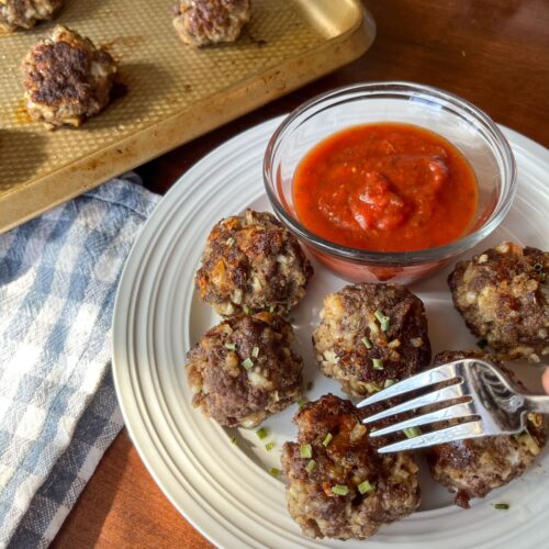 Eggless meatballs on a plate with a side of sauce. Some meatballs also on a baking sheet.
