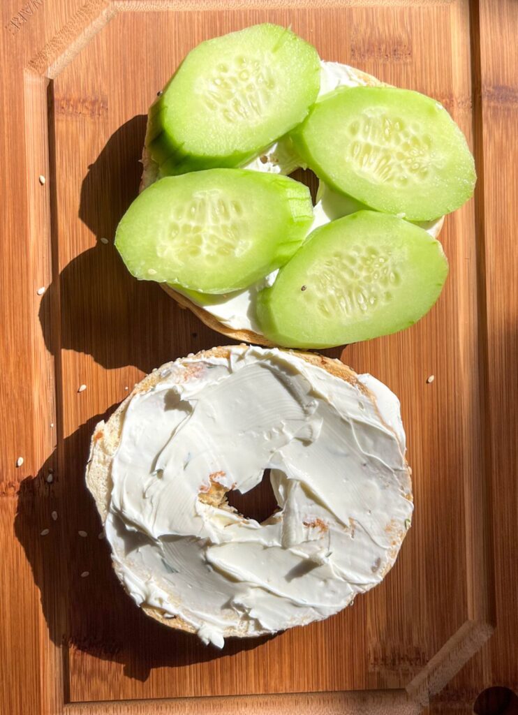 Cream cheese on a bagel and sliced cucumbers layered on