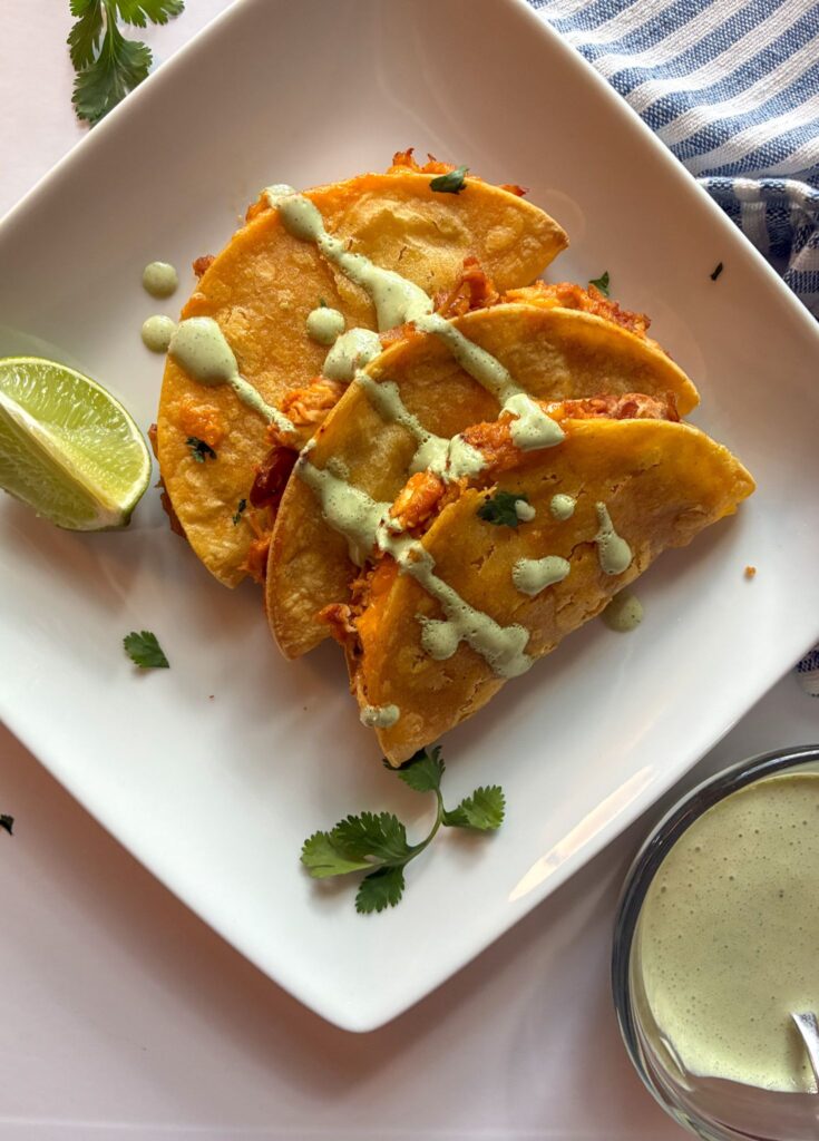Baked chicken tacos on a plate drizzled with cilantro lime sauce