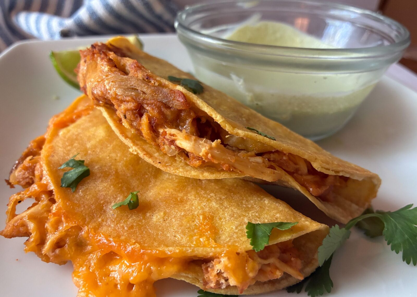 Two baked chicken tacos with a side of cilantro lime sauce in a bowl