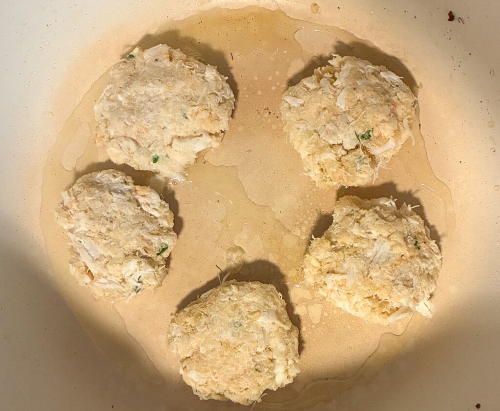 5 crab cakes in a frying pan being cooked